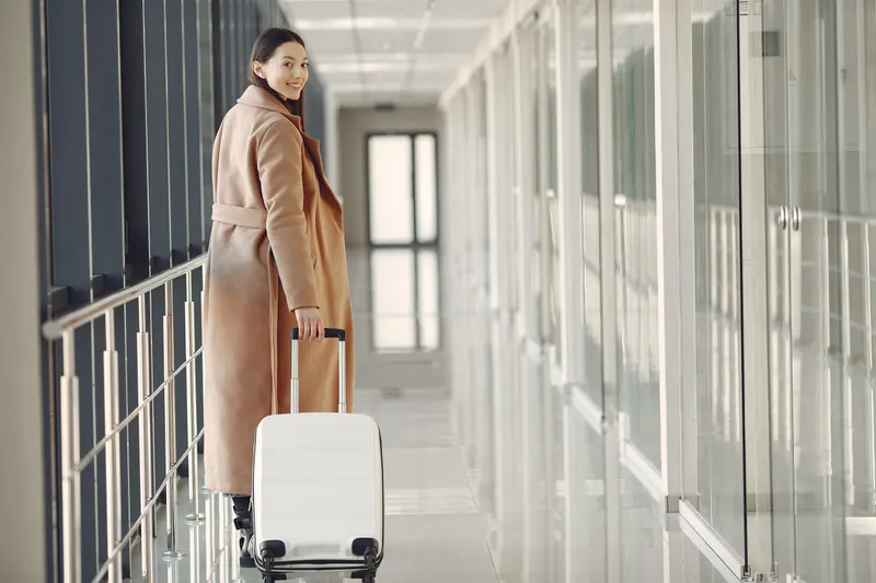 Mulher sorrindo, olhando para trás, enquanto puxa uma mala num corredor de aeroporto